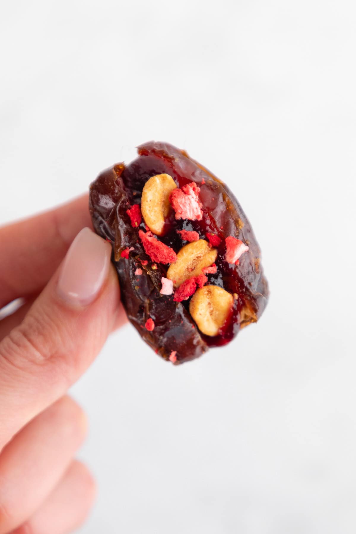 a hand holding a medjool date stuffed with peanut butter, jam, peanuts, and fruit