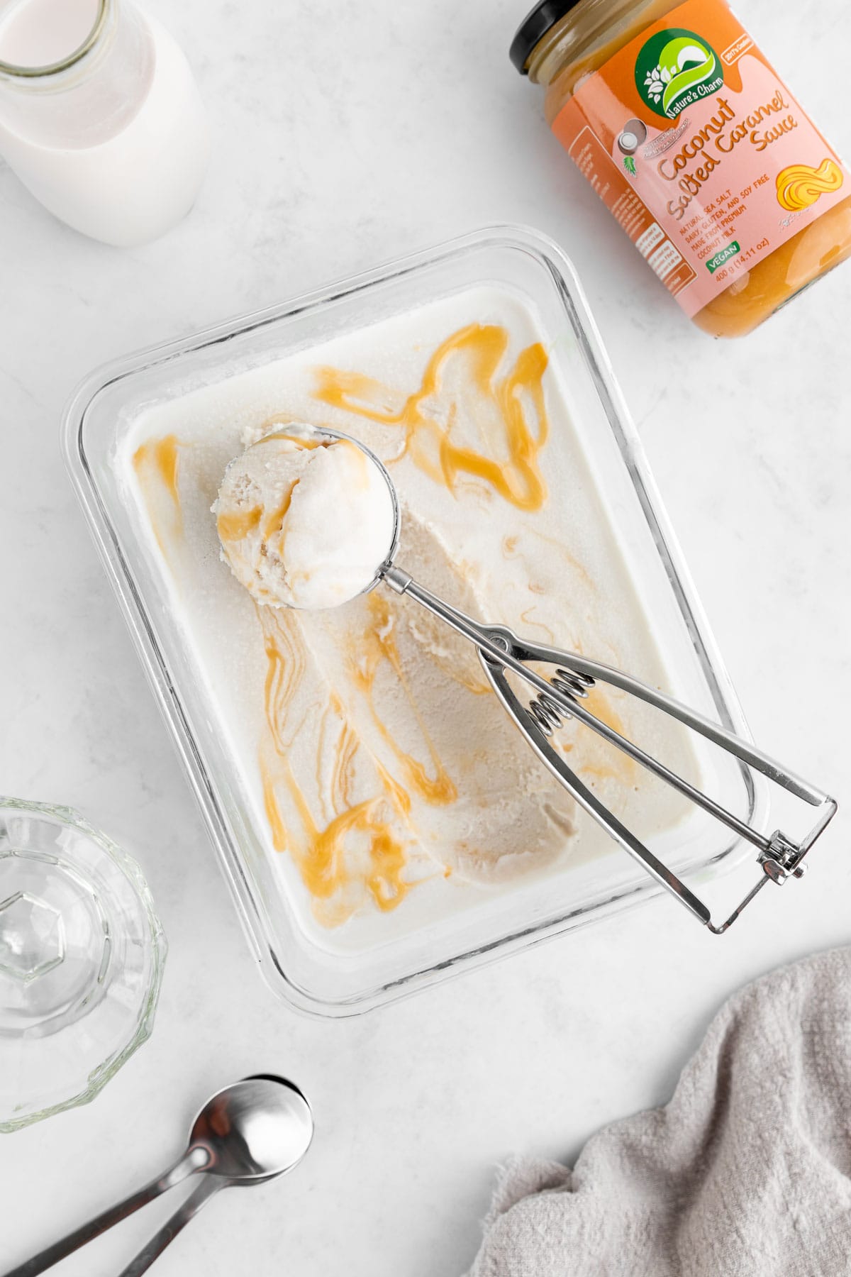 an ice cream scoop scooping vegan salted caramel ice cream out of a glass dish