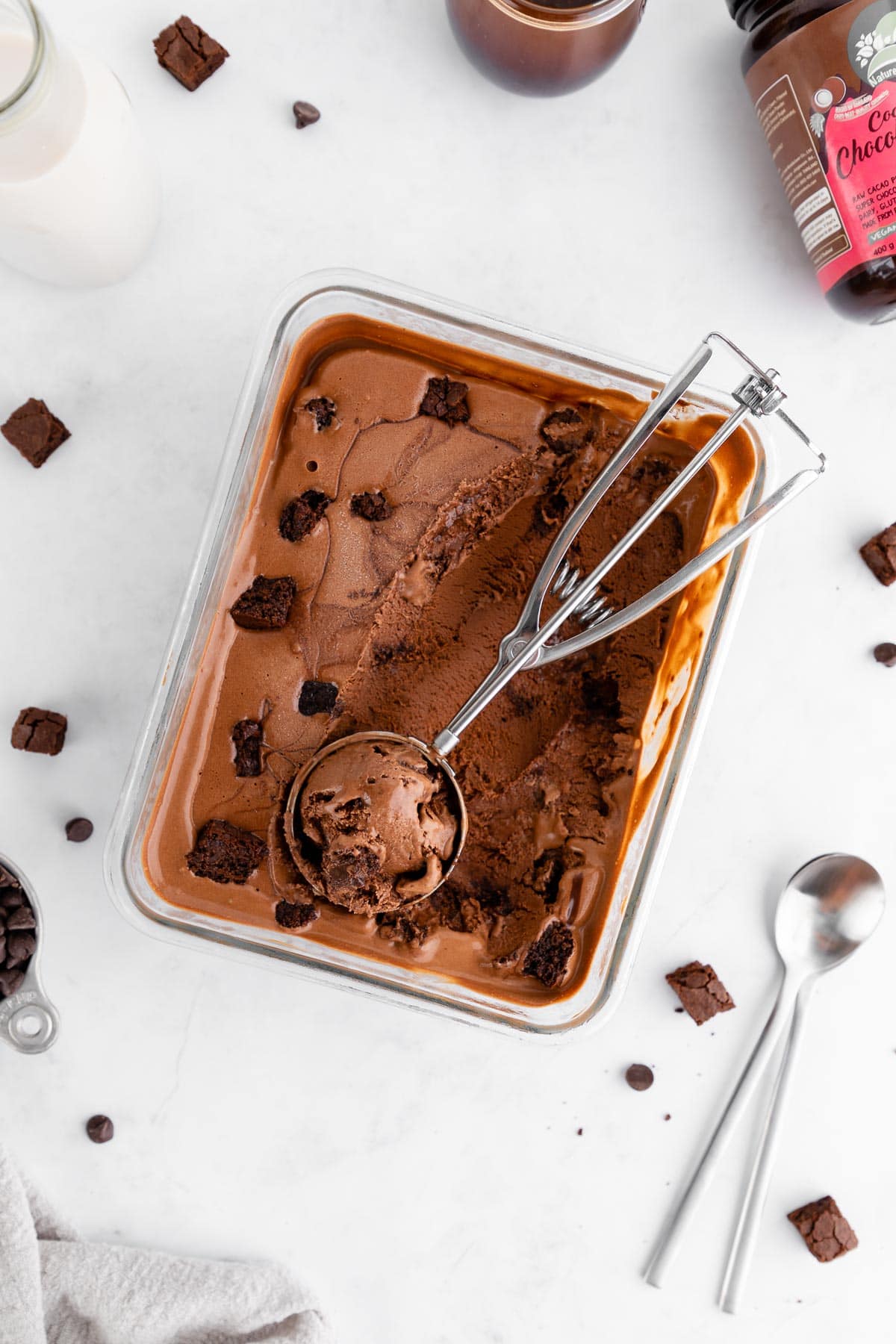 scooping vegan chocolate fudge brownie ice cream inside a glass container