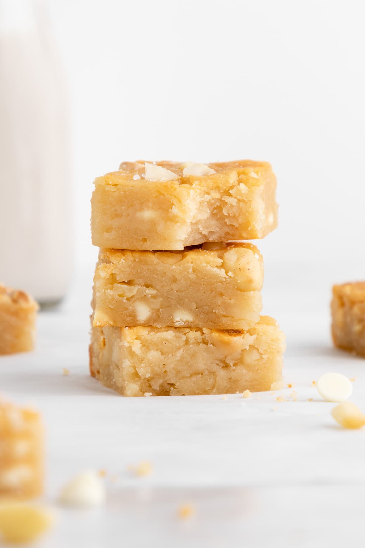 a stack of vegan white chocolate macadamia nut blondies with a bite taken out of the top one
