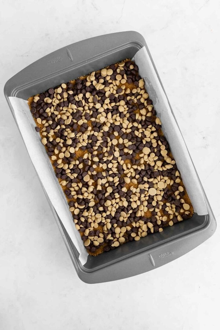 chocolate chips and butterscotch chips over graham cracker crust inside a 9x13 baking pan