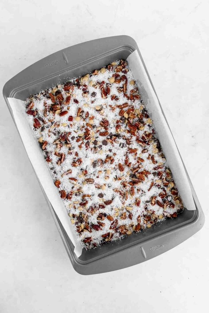 chocolate chips, butterscotch chips, pecans, and shredded coconut on top of graham cracker crust inside a 9x13 baking pan